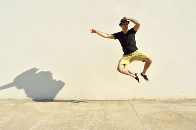 Full length of young man jumping on footpath against wall