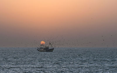 Boat sailing in sea against sky during sunset