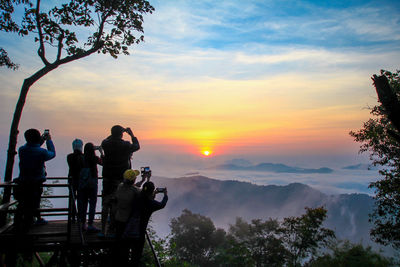 People looking at mountains against sky during sunset