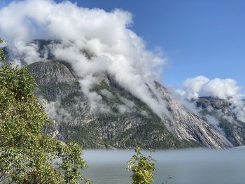 Scenic view of fjord against mountain covered in clouds with clear sky above