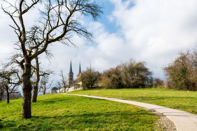 Road passing through grassy field against cloudy sky