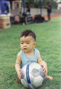 Cute boy with ball sitting on field