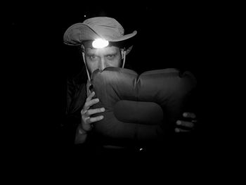 Midsection of man wearing hat sitting against black background