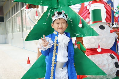 Portrait of smiling boy wearing crown while standing by christmas tree in party
