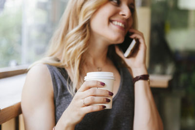 Midsection of woman talking over mobile phone while sitting in cafe