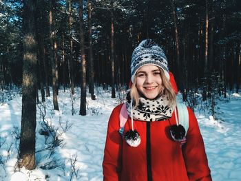 Portrait of smiling young woman standing in forest during winter