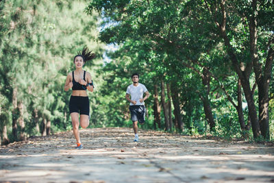 Full length of determined woman and man jogging on road amidst trees