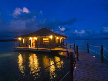 Illuminated building by sea against sky at night