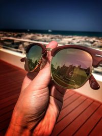 Cropped image of hand holding sunglasses against sea