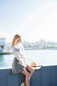 Woman sitting on railing of ship in sea against sky