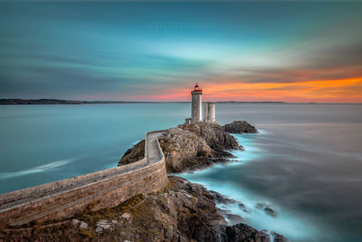 Lighthouse by sea against sky during sunset