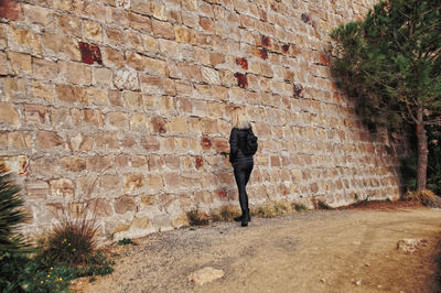 Full length rear view of woman walking against brick wall