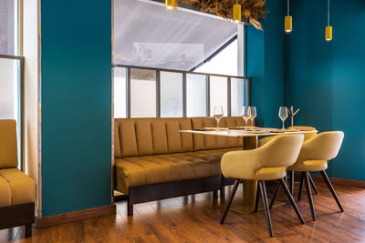 Sofa and comfortable armchairs at table with wineglasses and plates prepared for guests of stylish restaurant