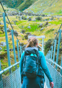 Rear view of female hiker walking on footbridge against mountains