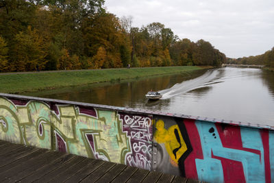 Graffiti on tree by water against sky