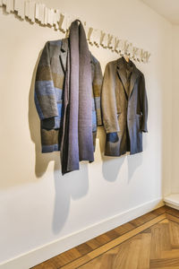 Trendy gray coats for men with stylish dark scarf hanging on hooks at white wall in light room of apartment