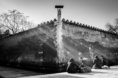 People sitting by historic building against sky