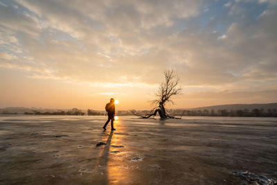 Man standing on frozen lake against sky during sunset