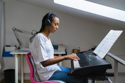 Teenage girl playing piano while sitting at home