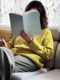 Midsection of woman reading book while sitting on sofa at home