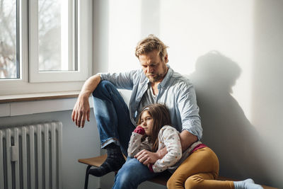 Girl resting on father's lap sitting at home