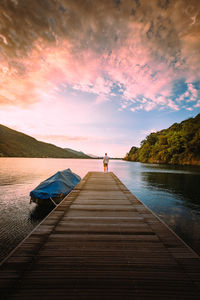 Young man watching the sun rise on the wooden jetty of lake mergozzo