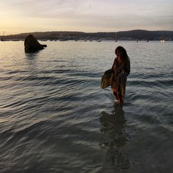 Woman with umbrella on sea against sky during sunset
