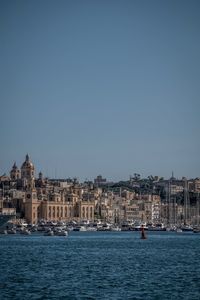 Boats in sea by buildings against clear sky