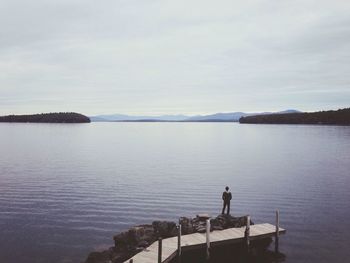 Rear view of a man standing on jetty overlooking sea