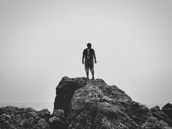 Rear view of man standing on rock against clear sky