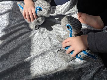 Cropped hands of children playing with stuffed toys on bed at home