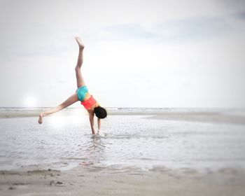 Rear view of girl doing cartwheel on shore at beach against sky