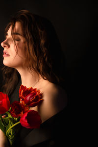 Close-up of young woman holding rose against black background