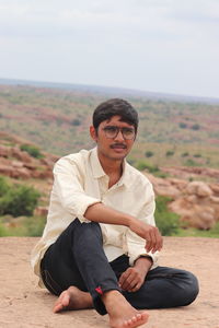 Portrait of young man sitting on land against sky