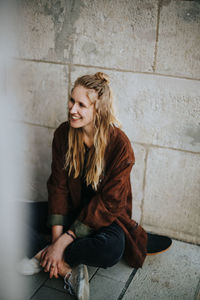 Smiling young woman sitting against wall