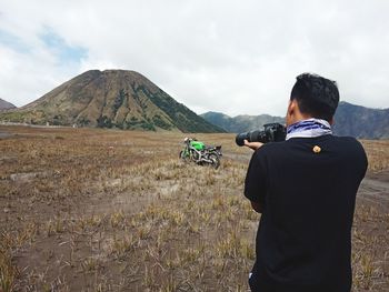 Rear view of man photographing through camera while standing on field at bromo tengger semeru national park
