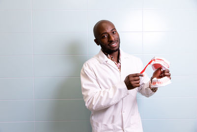 Portrait of dentist standing against wall