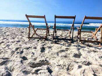 Deck chairs on beach against sky