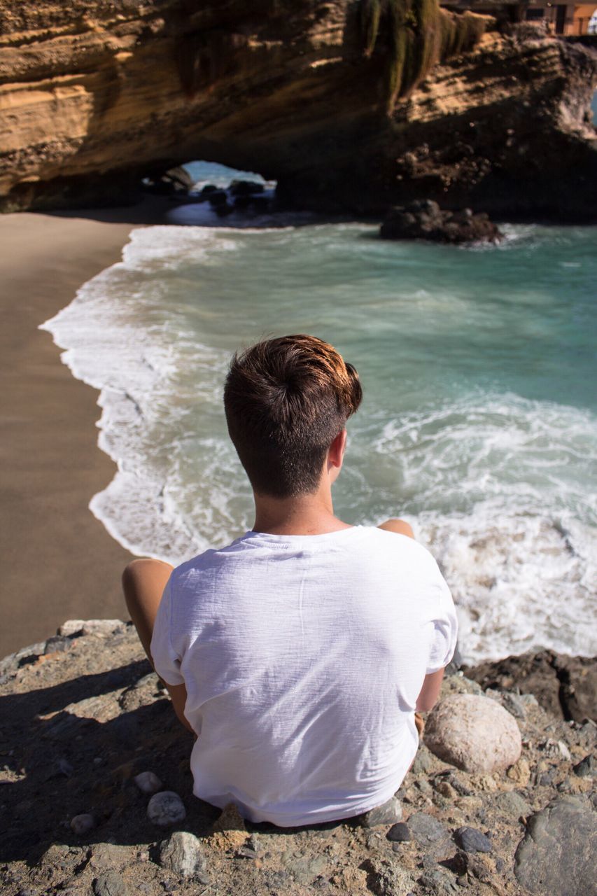 water, rock - object, rear view, lifestyles, leisure activity, beach, standing, shore, nature, day, full length, outdoors, sea, relaxation, sitting, casual clothing, high angle view, stone - object