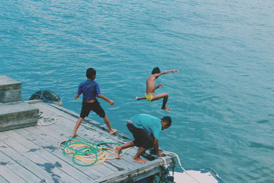 High angle view of playful boys jumping in sea from pier at beach