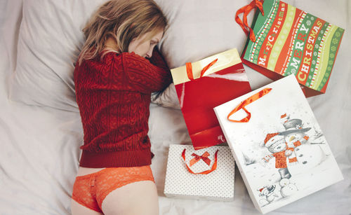 Directly above shot of woman sleeping with christmas presents on bed