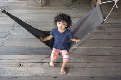 Full length portrait of girl sitting on hammock over wooden floor