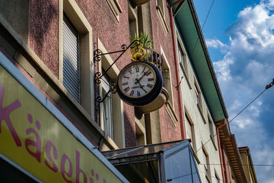 Low angle view of clock hanging on building against sky