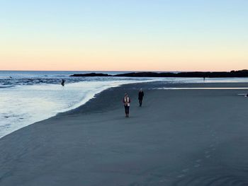 People at beach against clear sky during sunset