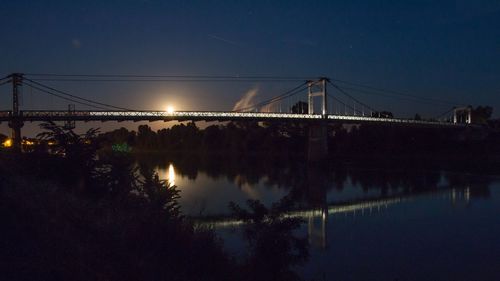 Illuminated bridge over river against sky at night