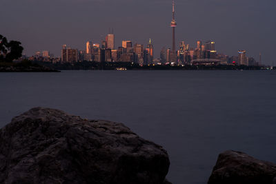 Sea by buildings against sky at night in city