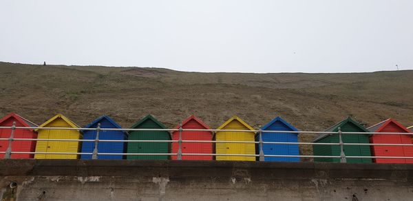 Multi colored huts on beach by buildings against clear sky