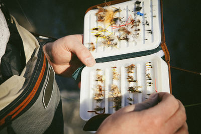 Midsection of man holding fishing hooks in box