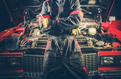 Midsection of mechanic with arms crossed standing by car in workshop