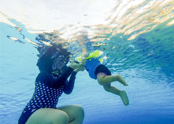 Low angle view of mother assisting toddler son swimming in sea